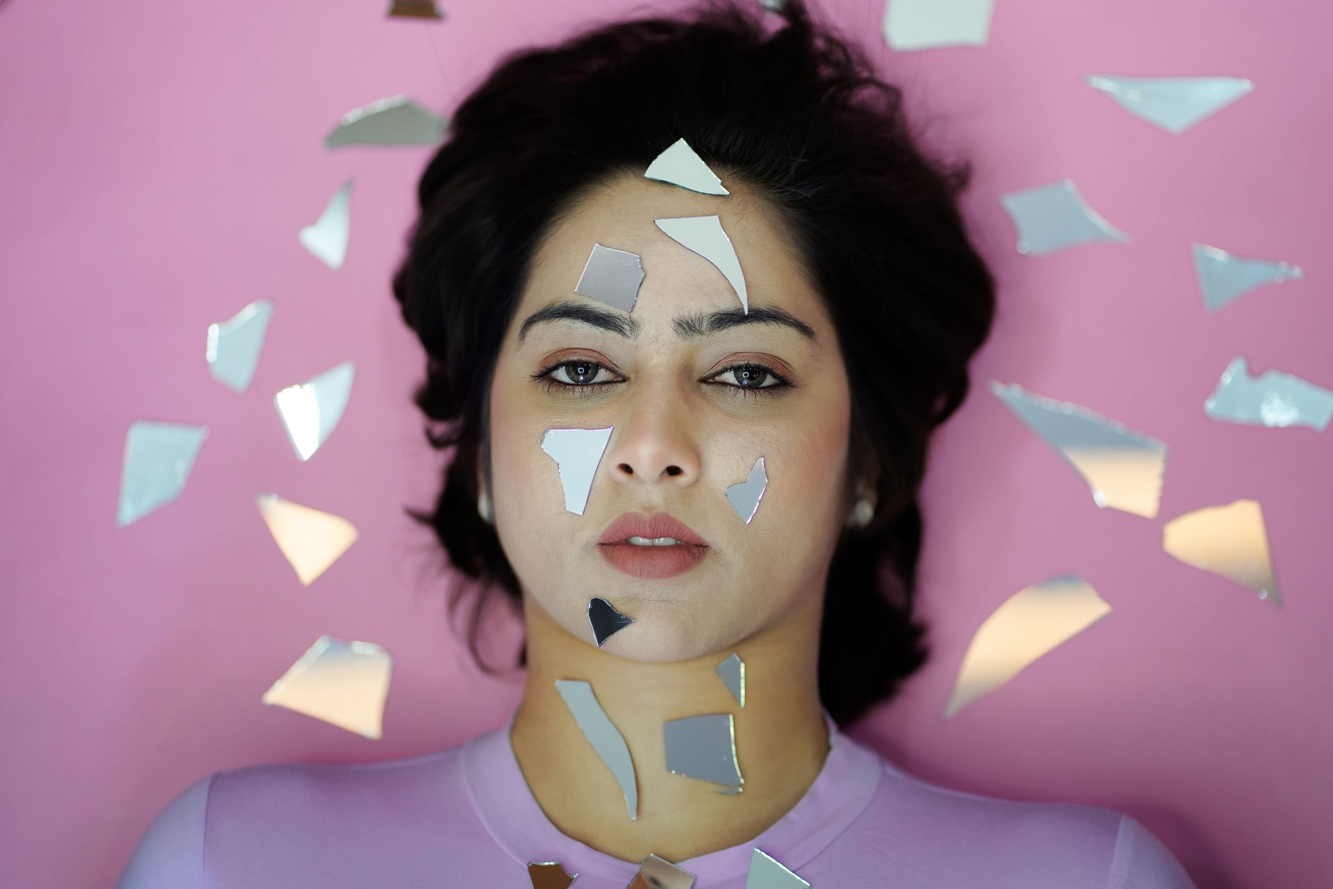 Artistic portrait featuring a woman with mirror shards on a pink backdrop, evoking creativity and reflection.