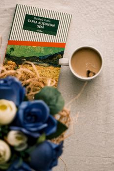 Flat lay of a book with coffee and blue roses on a table.