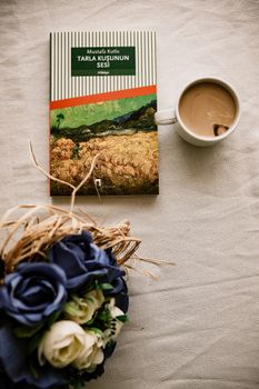 A book, coffee, and flowers on a table create a cozy atmosphere.