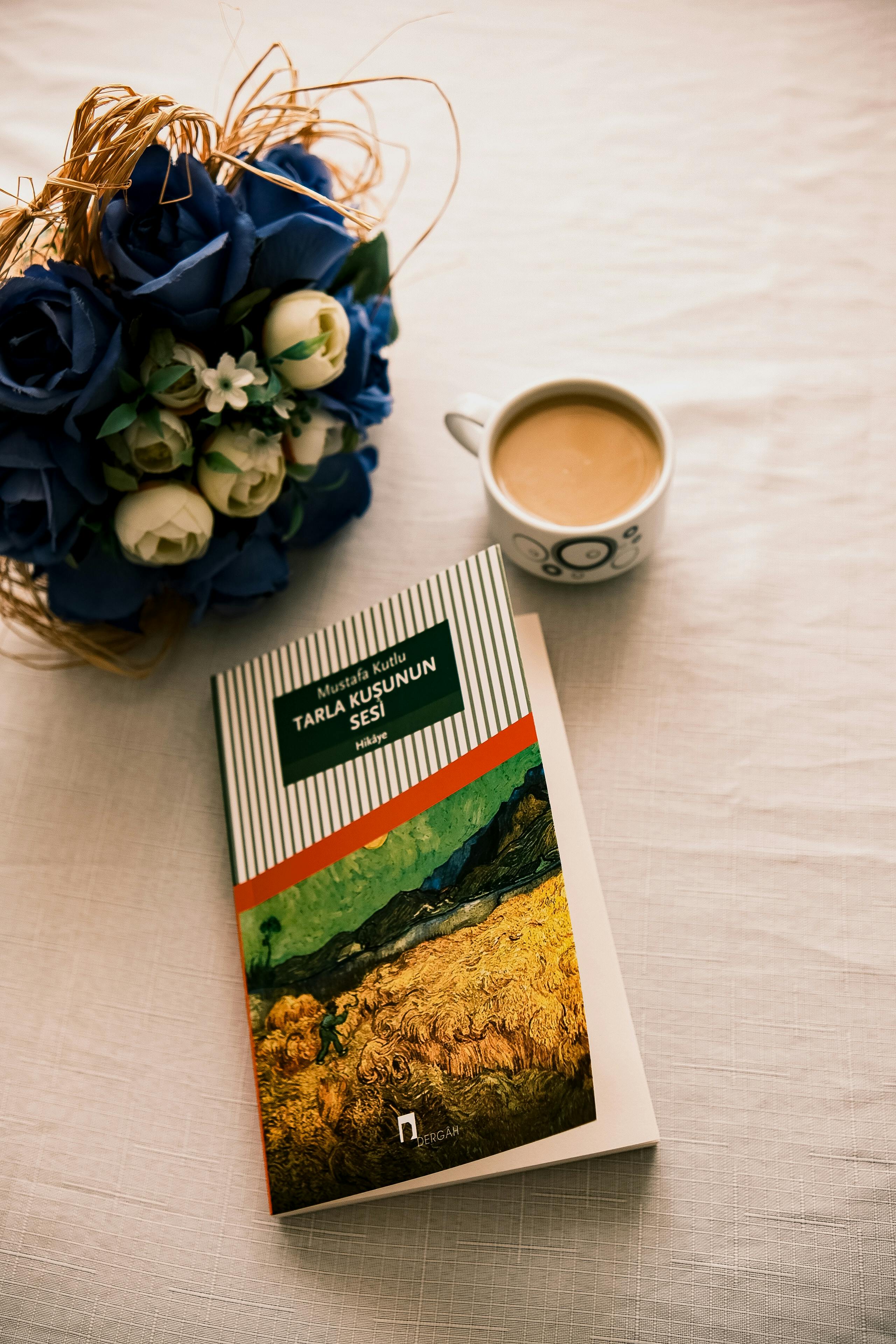 A cozy setup with a book, coffee, and floral bouquet on a table.