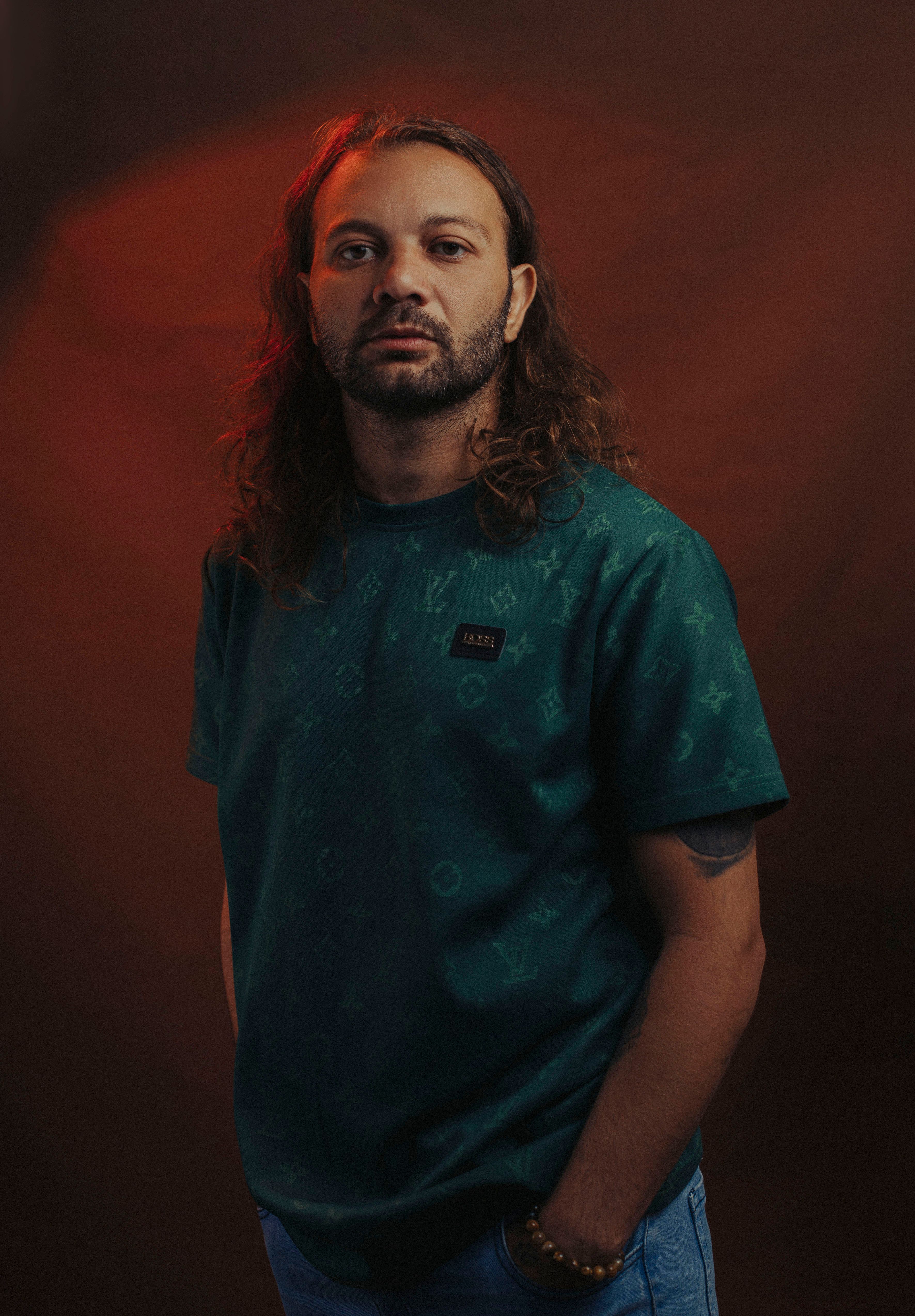 A thoughtful man with long hair wearing a green t-shirt, captured in a moody studio setting.