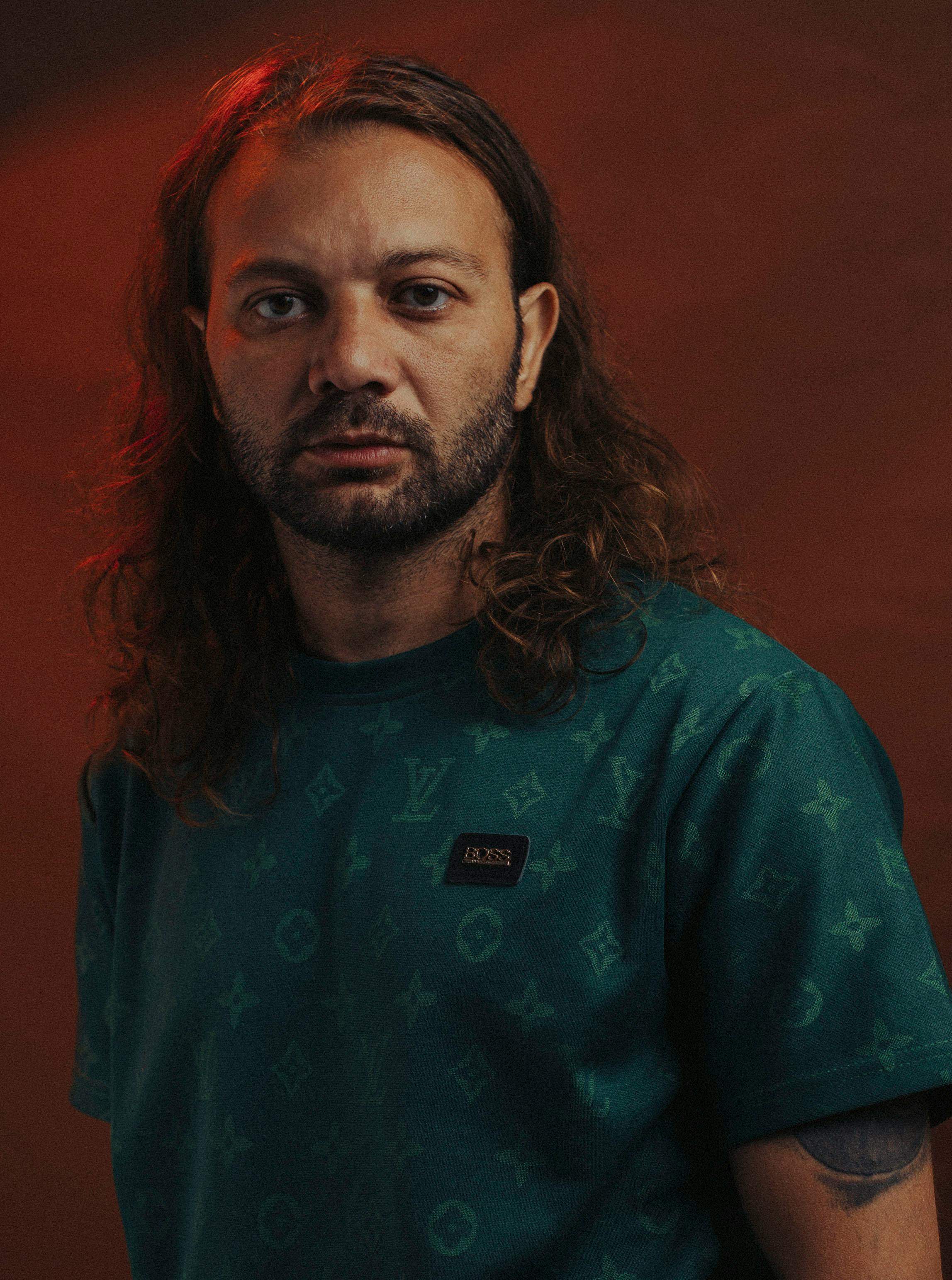 A contemplative man with long hair gazes directly, enveloped in dramatic, warm lighting.