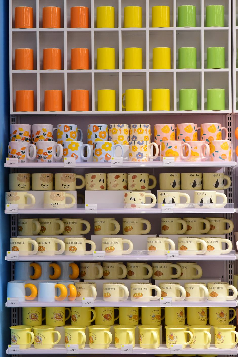 Colorful display of various mugs arranged by pattern and color on a neat shelf.