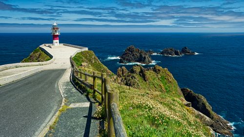Free A picturesque lighthouse on a cliff overlooking the rocky ocean coastline during the day. Stock Photo