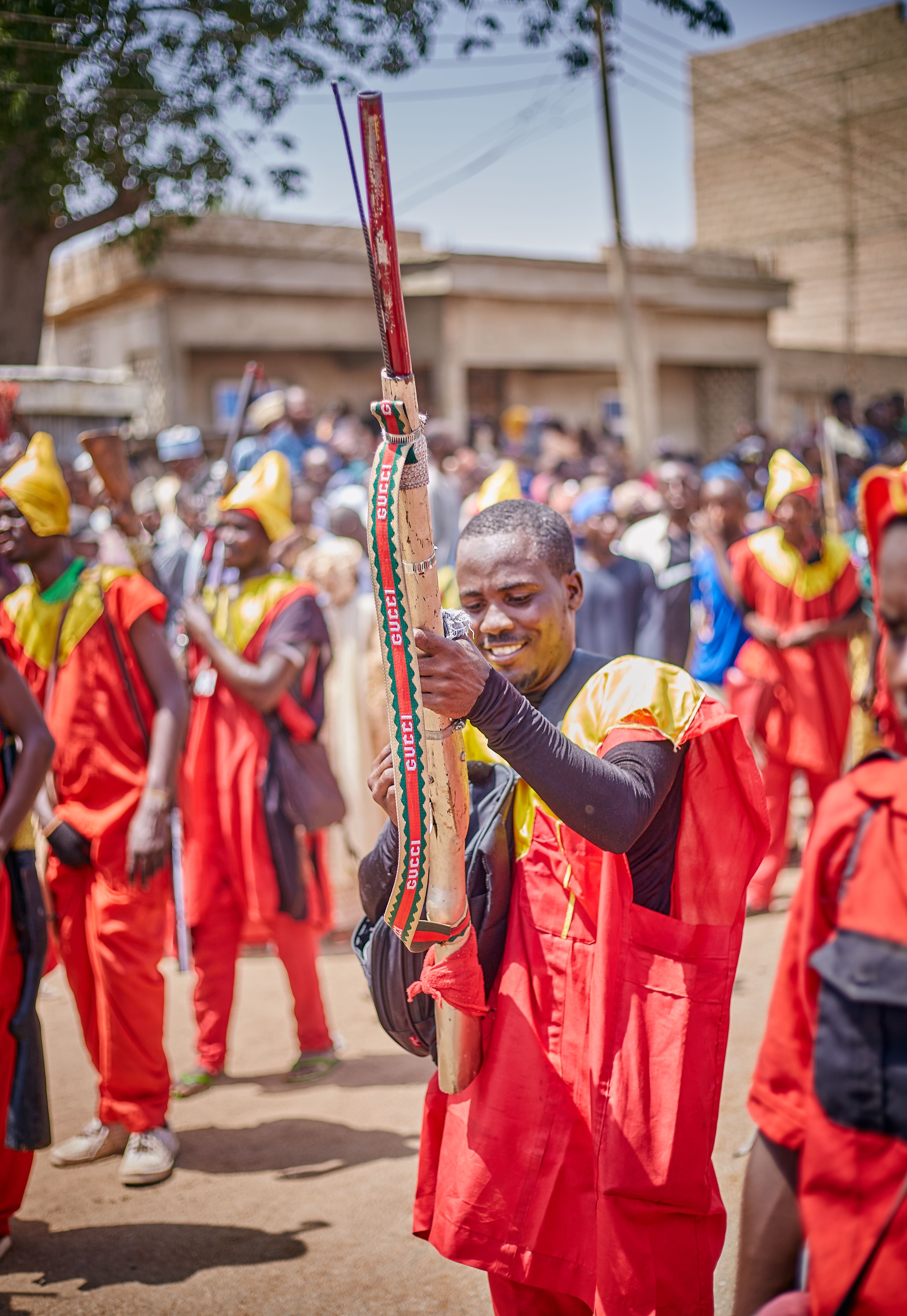 A lively festival scene with participants in traditional red attire holding decorated rifles.