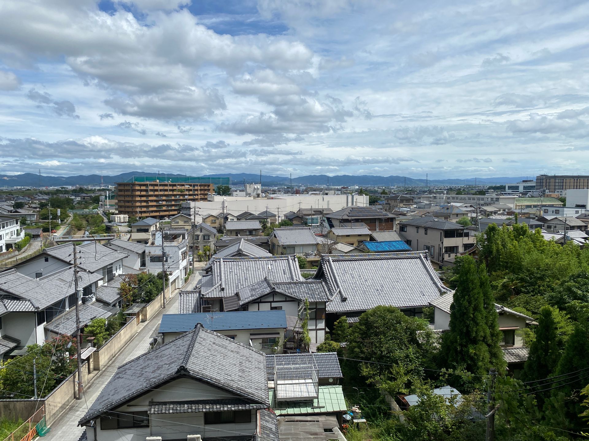 An aerial view of traditional Japanese homes with tiled roofs, set against a backdrop of mountains under a cloudy sky in Nara, Japan.