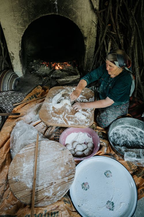Free Elderly woman making bread by an open fire, showcasing traditional baking techniques. Stock Photo