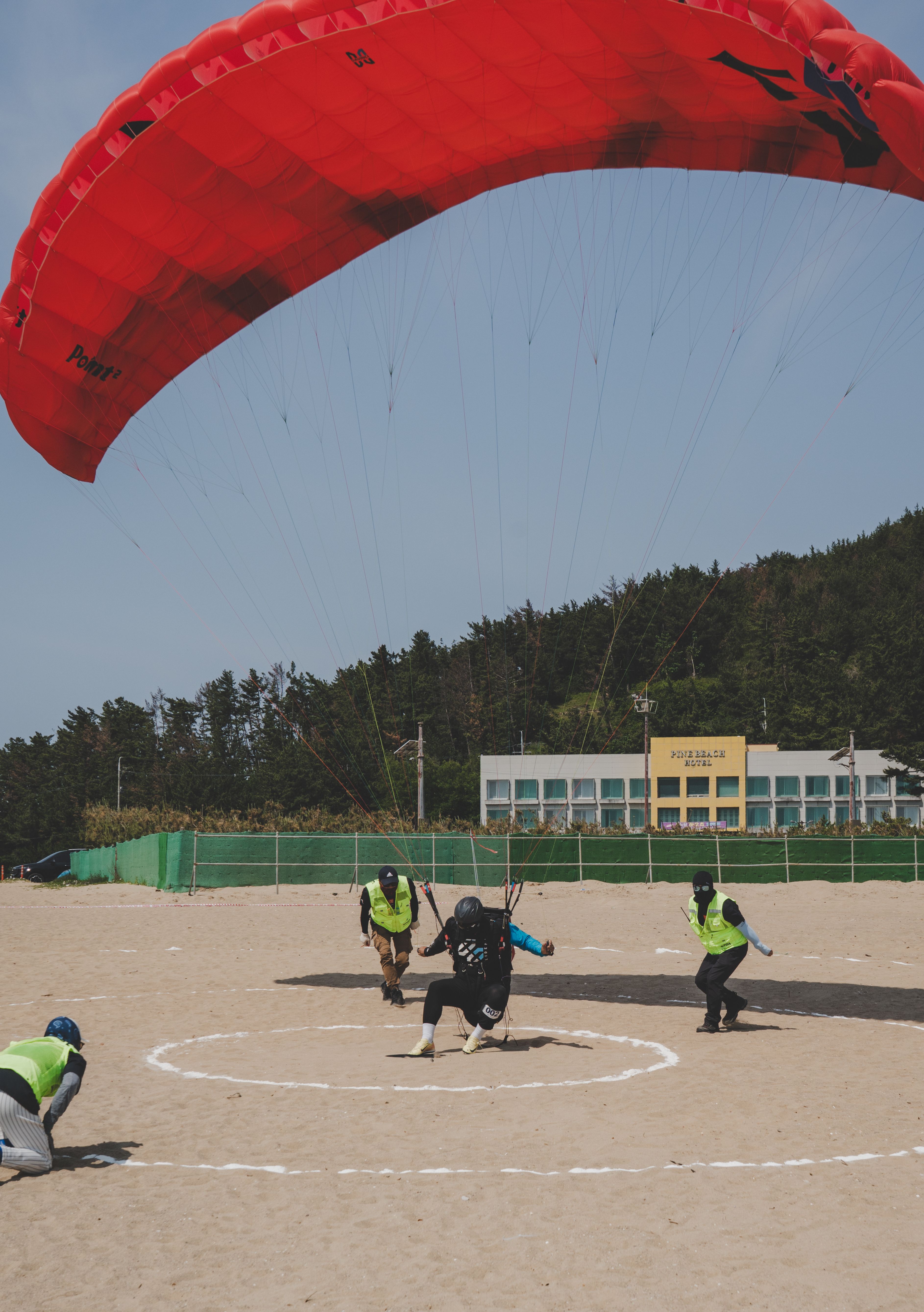 A paraglider makes a precise landing on a sandy beach, guided by instructors.