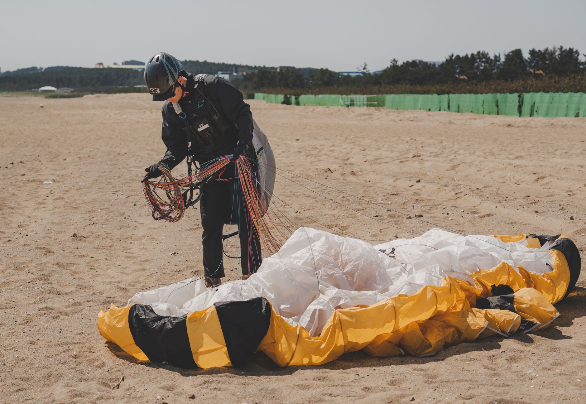Individual packing a paraglider on a sunny beach, organizing lines and equipment.