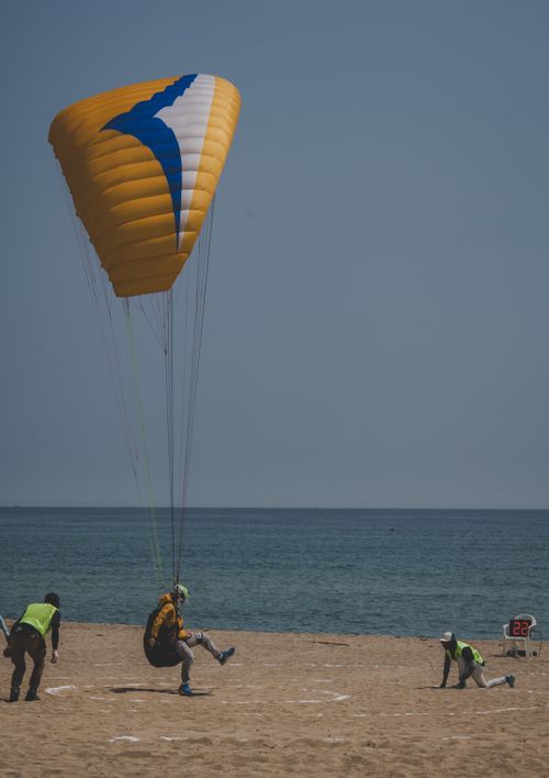 Free Paragliding landing on a sandy beach during a sporting event with several participants. Stock Photo