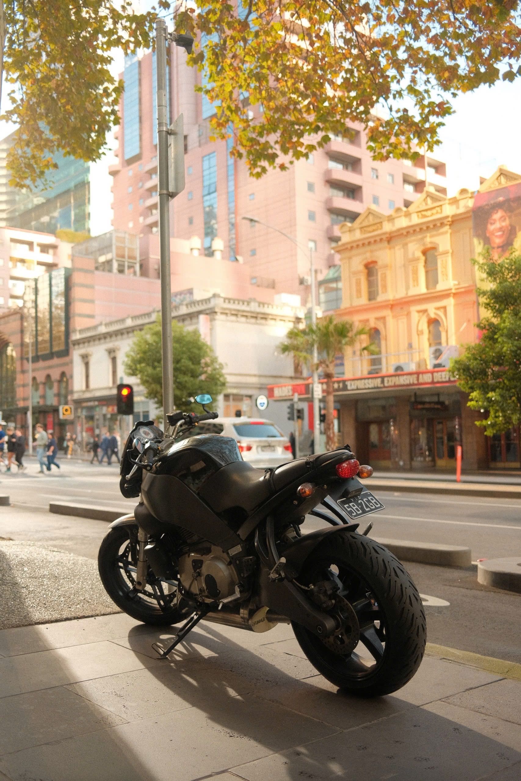 Motorcycle parked on city street with Melbourne architecture in the background.