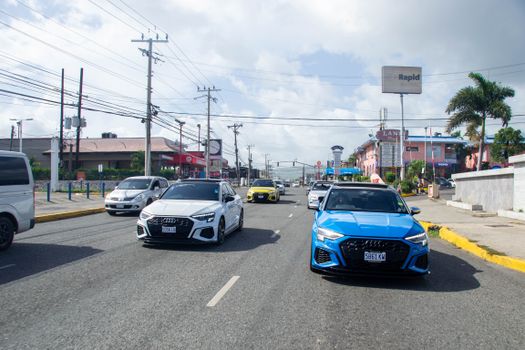 View of a bustling Jamaican street with various cars and local shops under bright daylight.