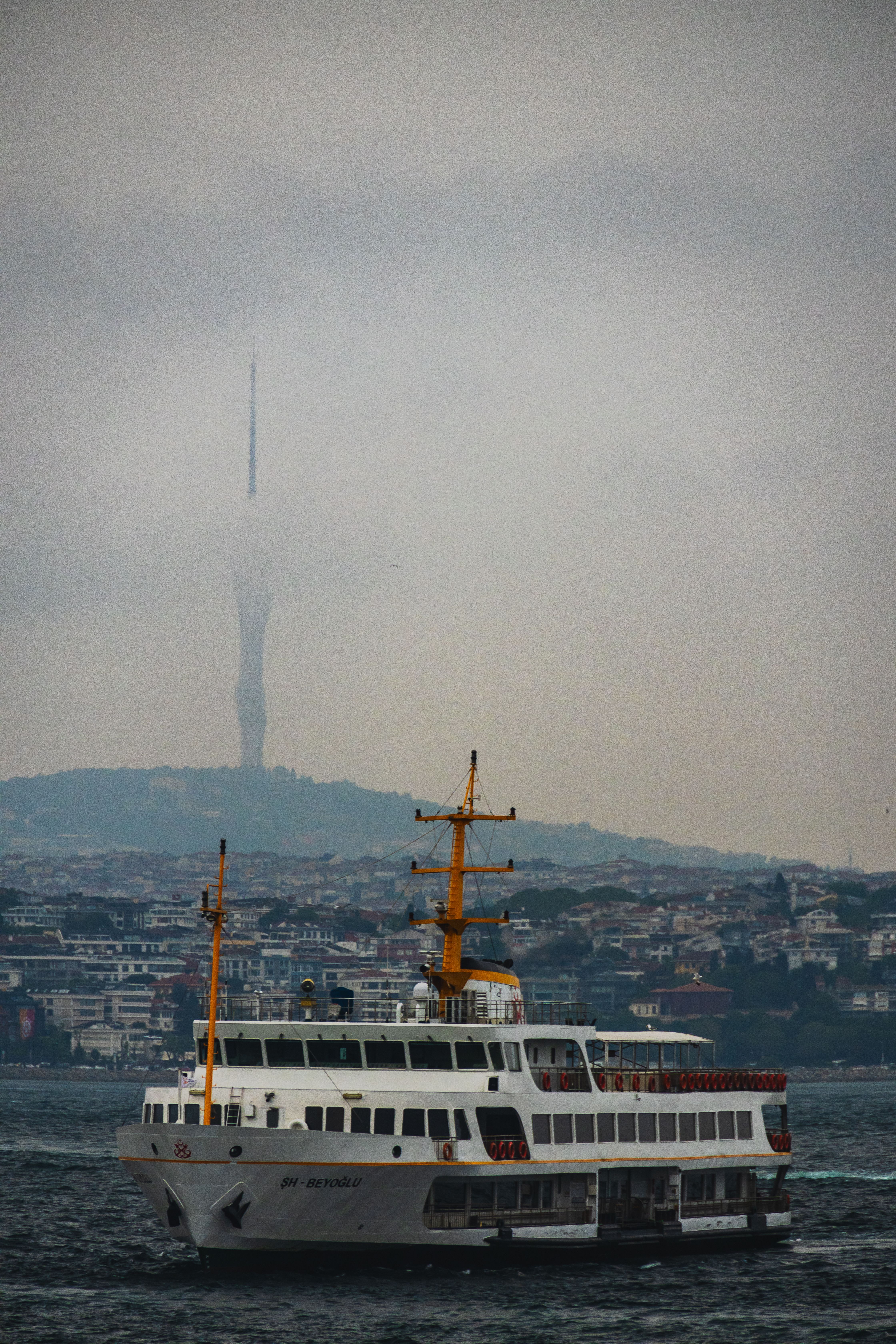Scenic view of ferry crossing Bosphorus with Camlica Tower shrouded in clouds, Istanbul.
