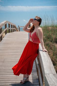 A fashionable woman in a red outfit basks in the summer sun on a Tybee Island boardwalk.