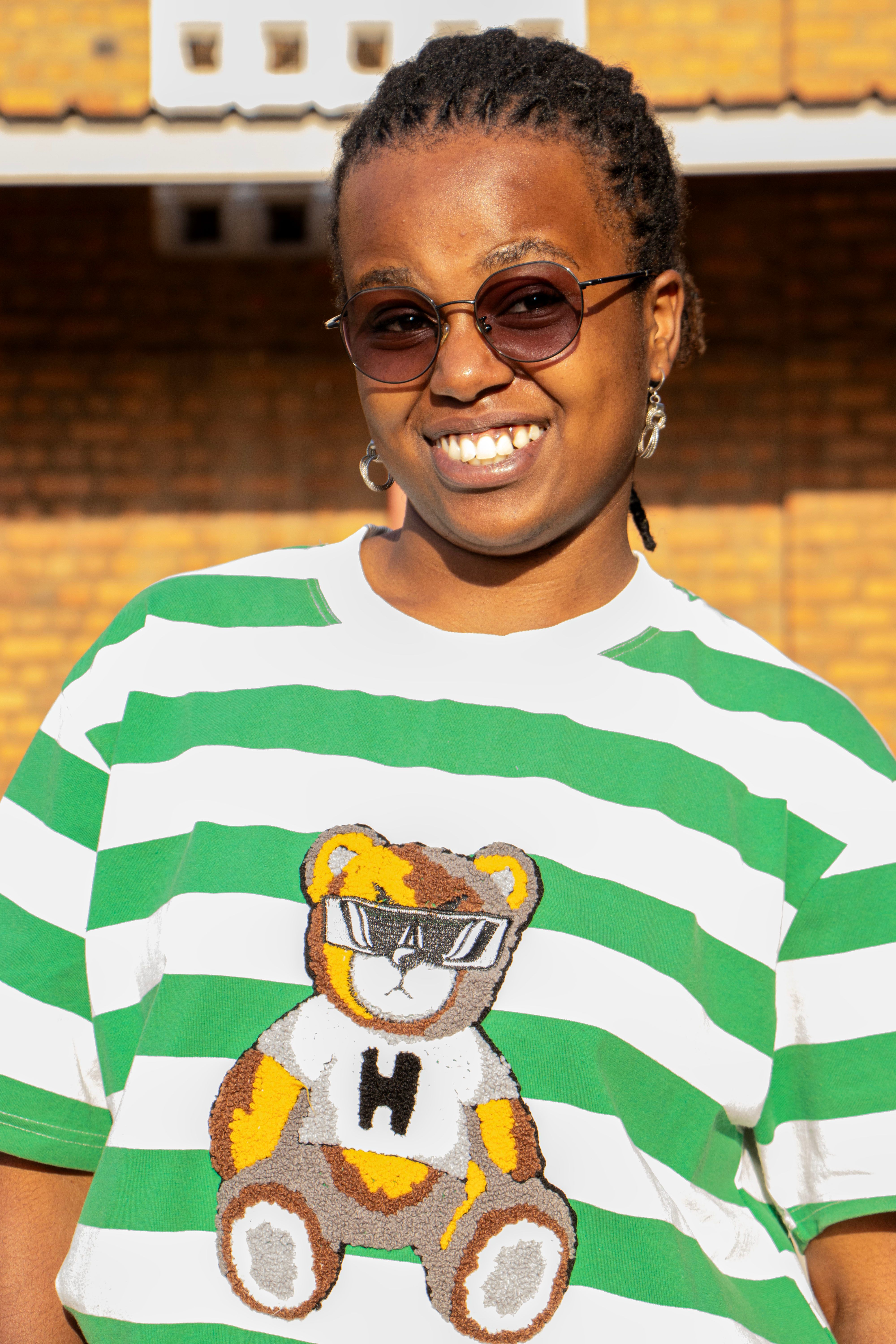 Person in sunglasses and striped T-shirt with bear graphic, smiling outdoors.