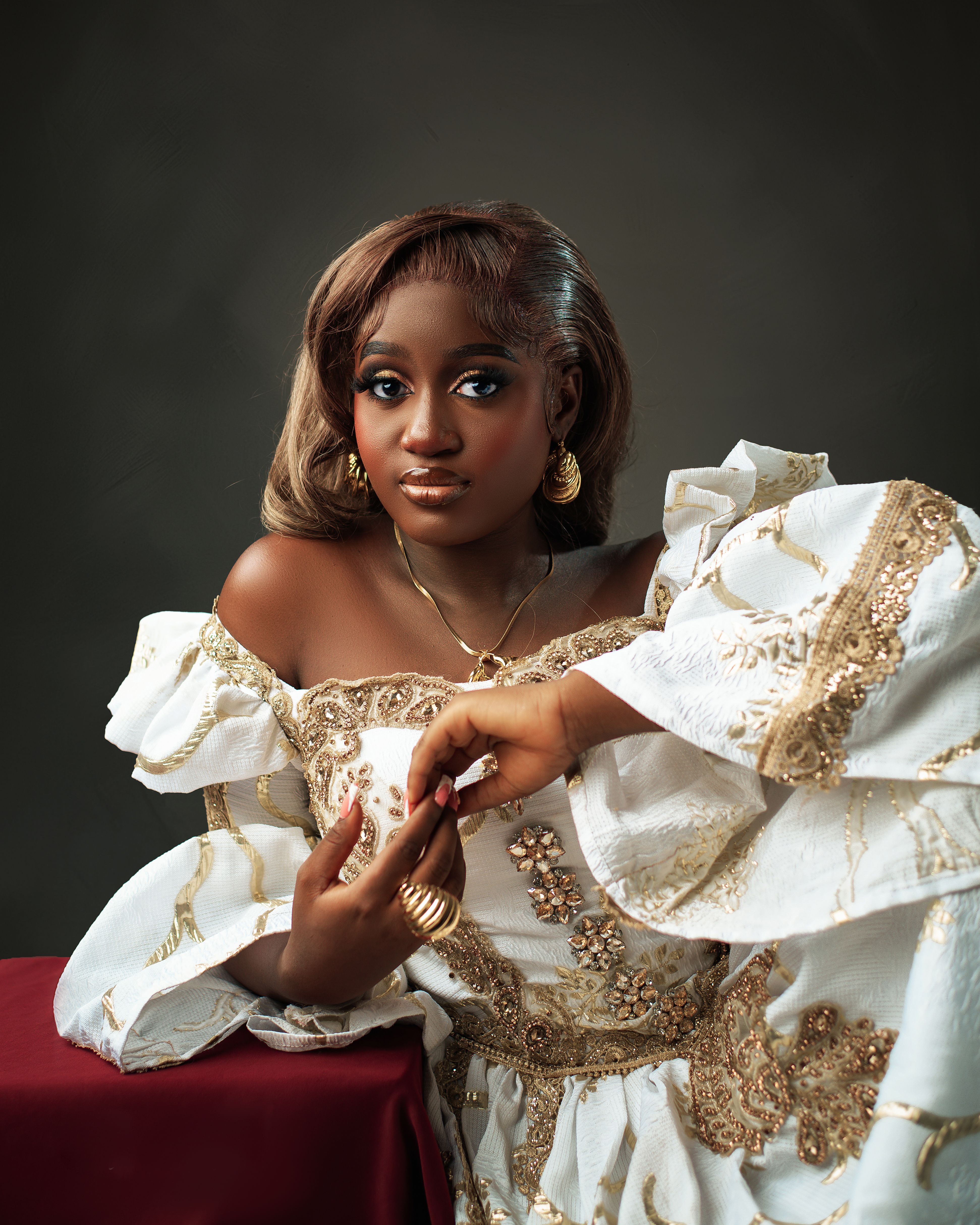 Portrait of a woman in a luxurious white and gold traditional dress, posed gracefully indoors.