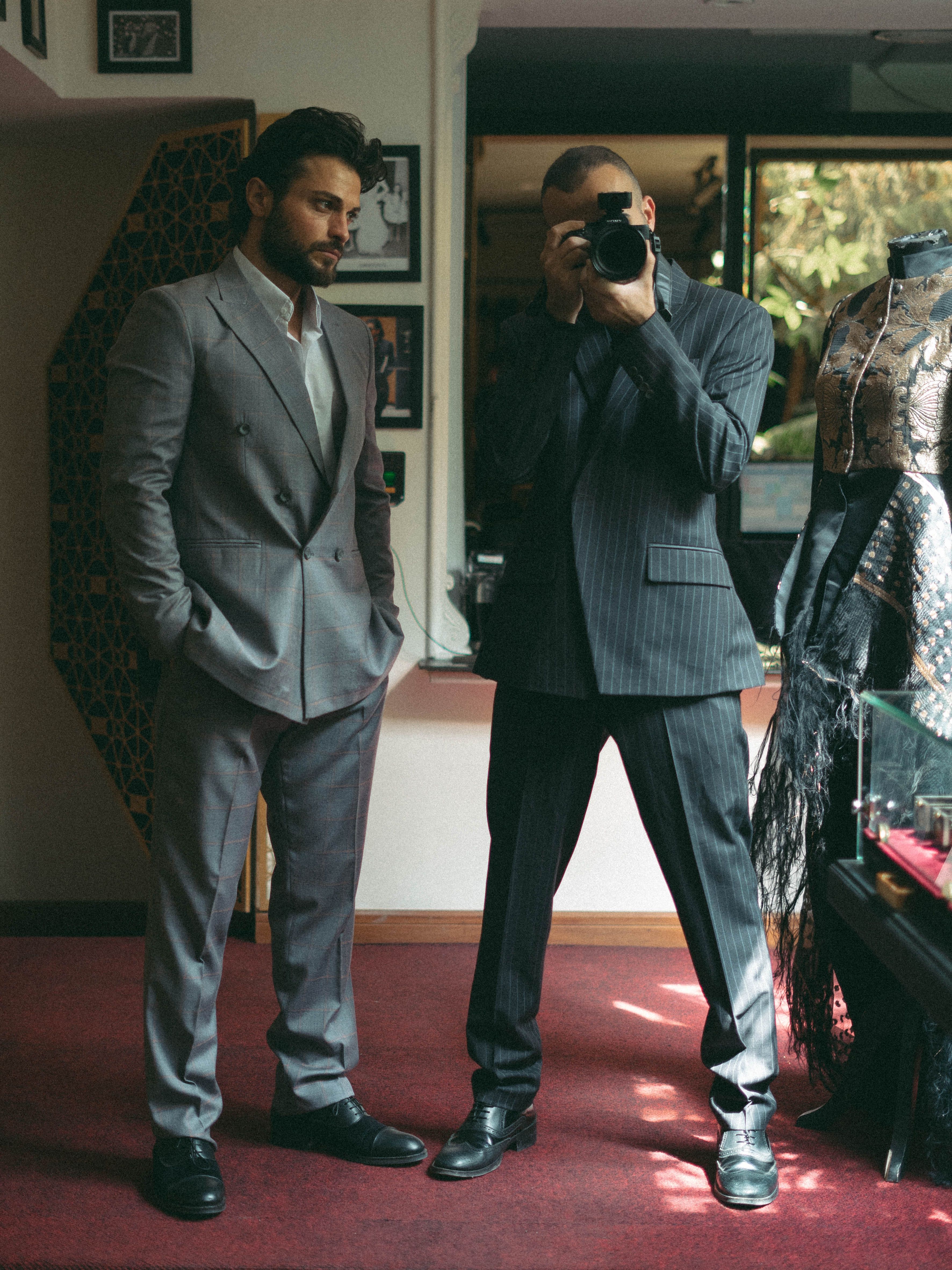 Photographer capturing model in stylish suits indoors, showcasing fashion and elegance.