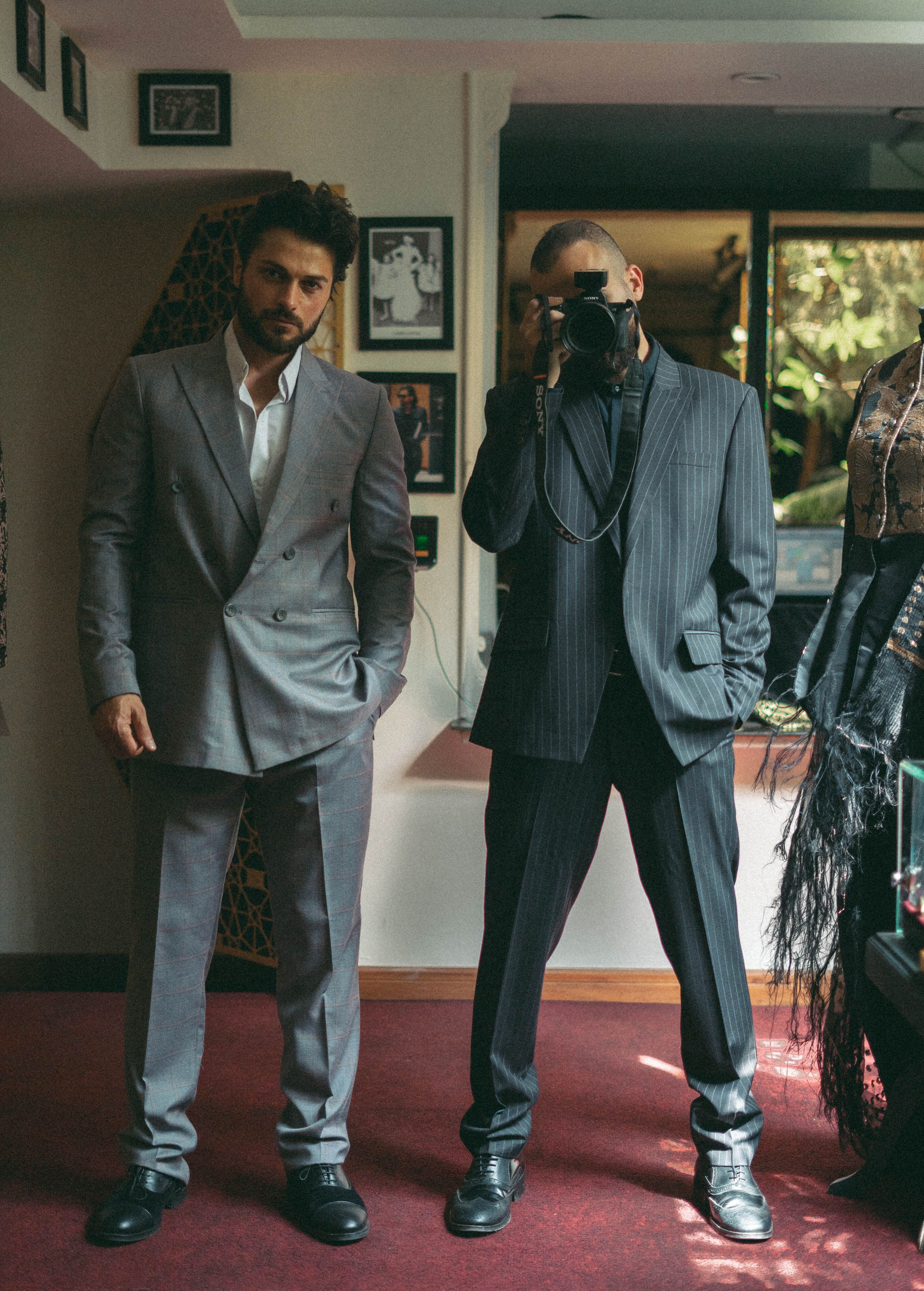 Two men pose in stylish suits indoors, capturing a sophisticated and modern vibe.
