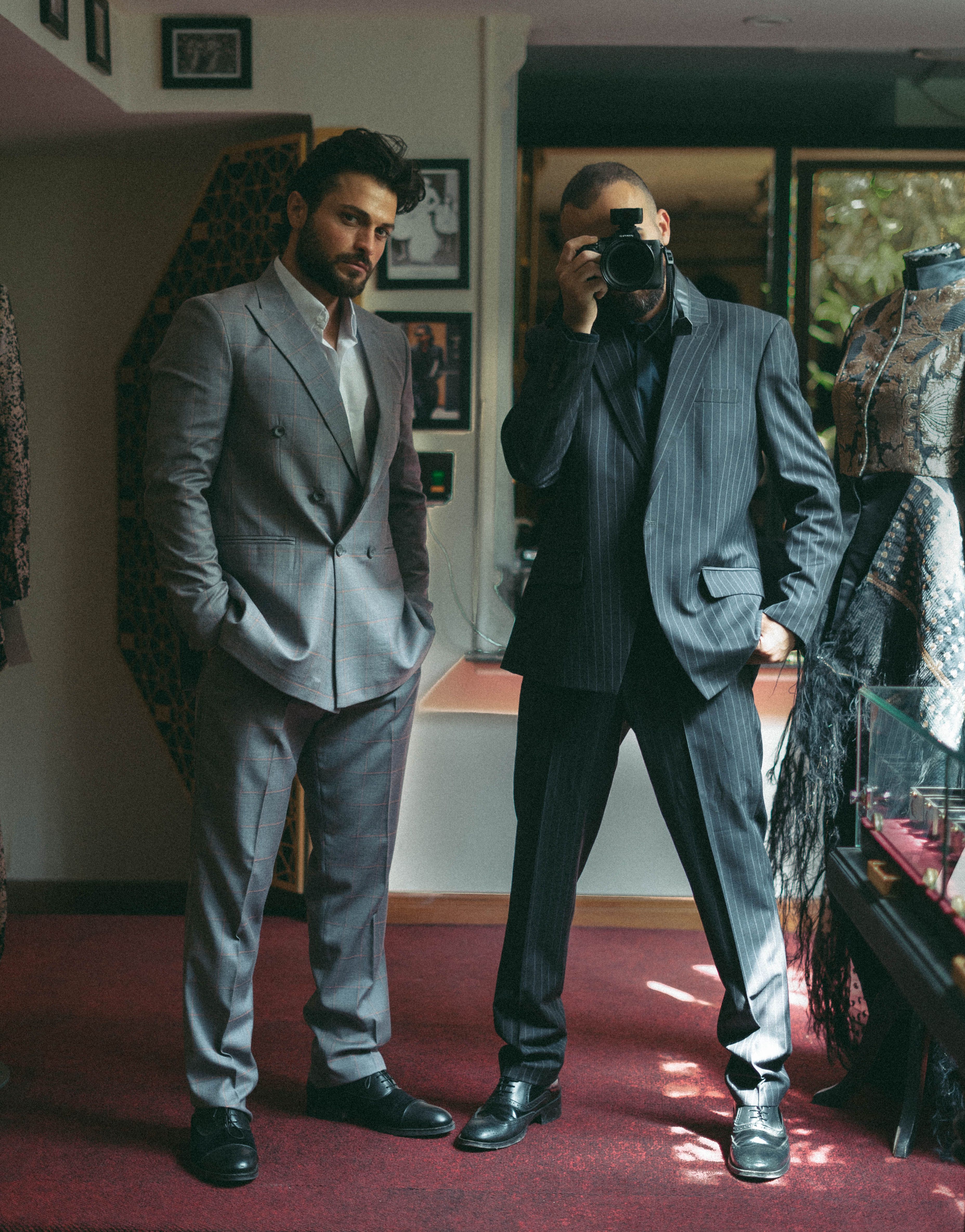Two men in elegant suits, one holding a camera, captured in a stylish indoor setting. - Key Factors to Consider When Choosing a Men's Dress