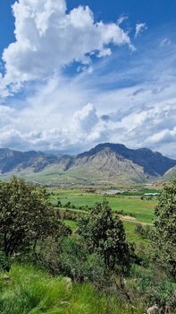 Vibrant mountain landscape with lush greenery under a dramatic blue sky and white clouds.