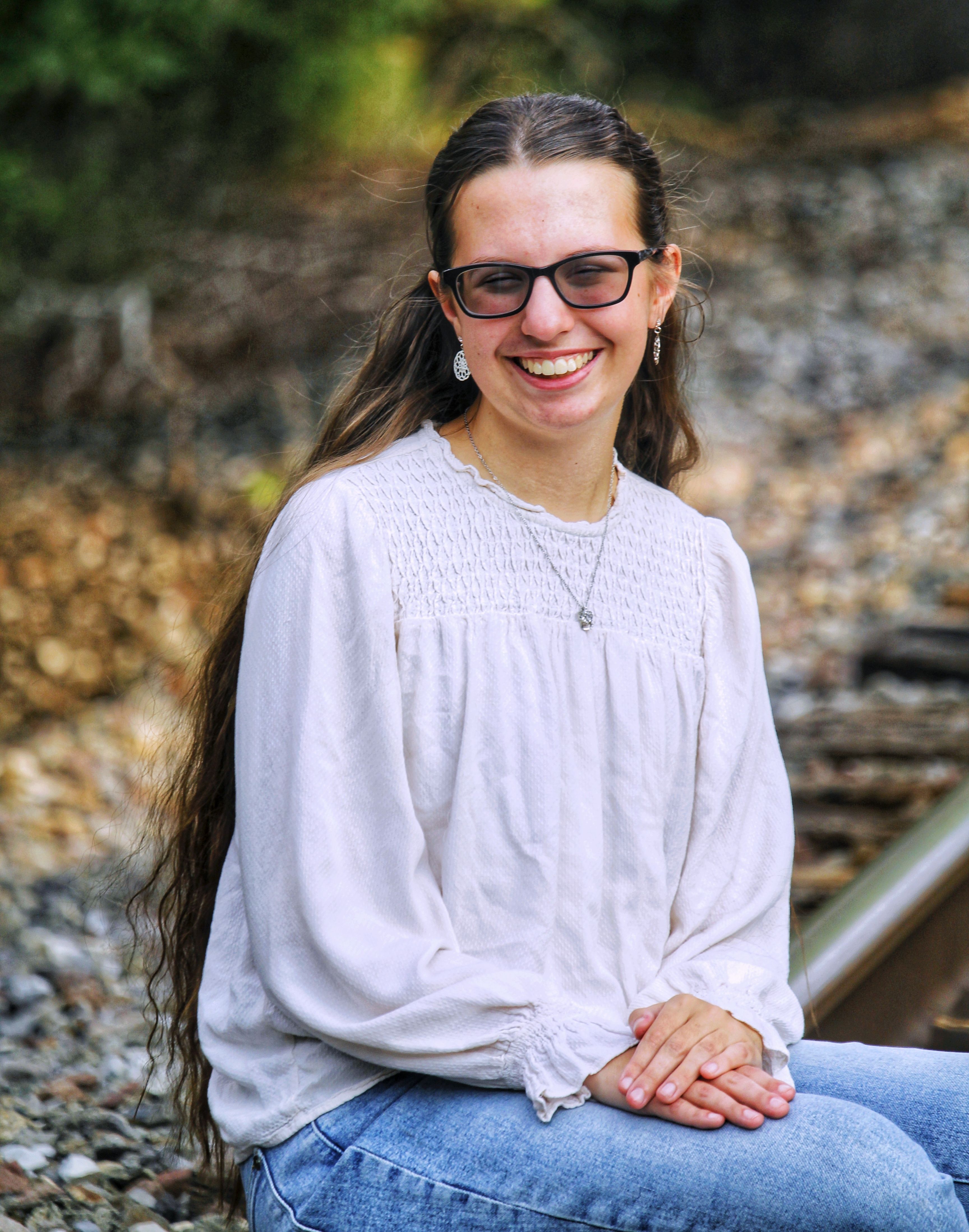 A cheerful woman with glasses sitting by the railroad tracks on a bright day.