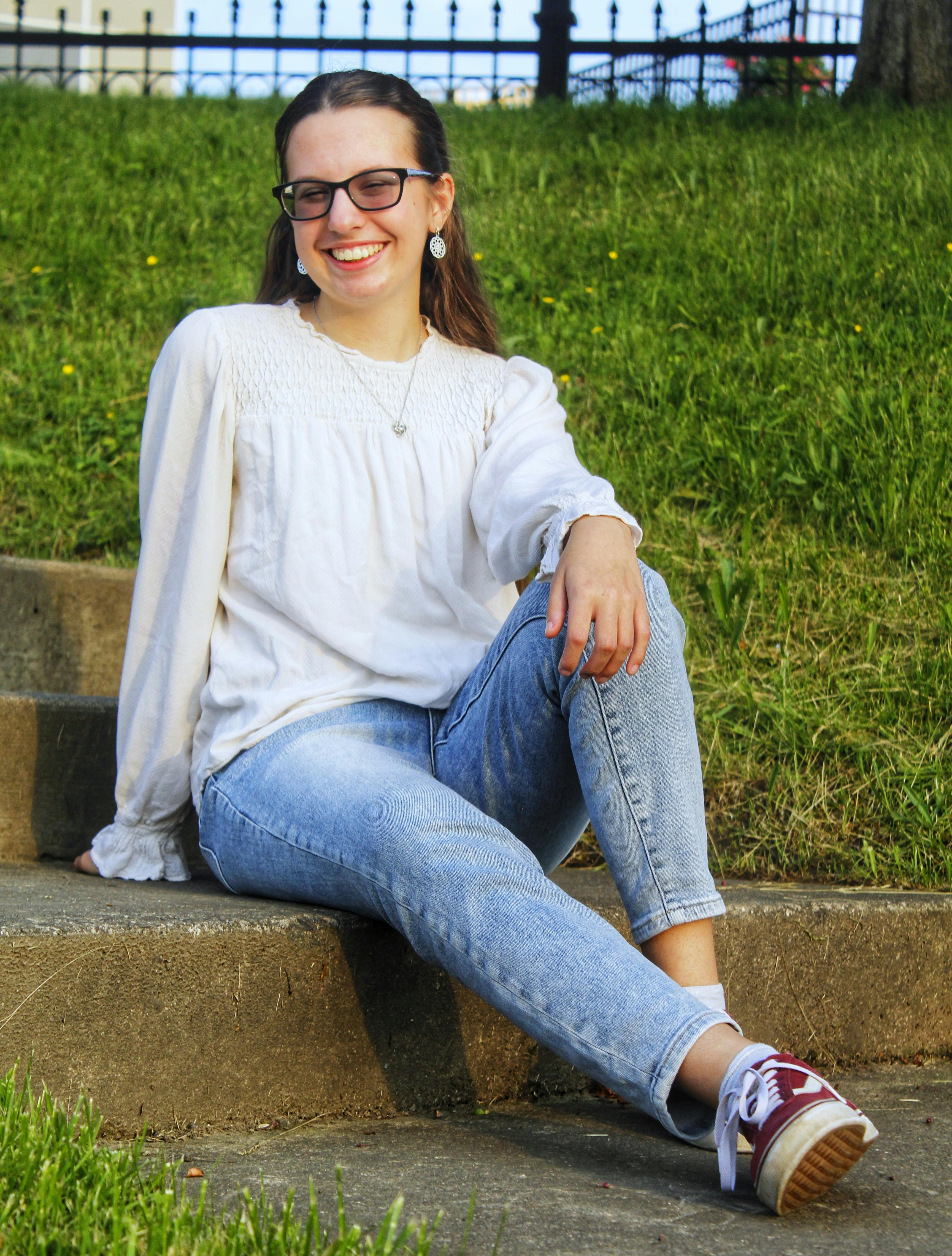 A cheerful woman sitting on outdoor steps against grassy backdrop, enjoying a sunny day.