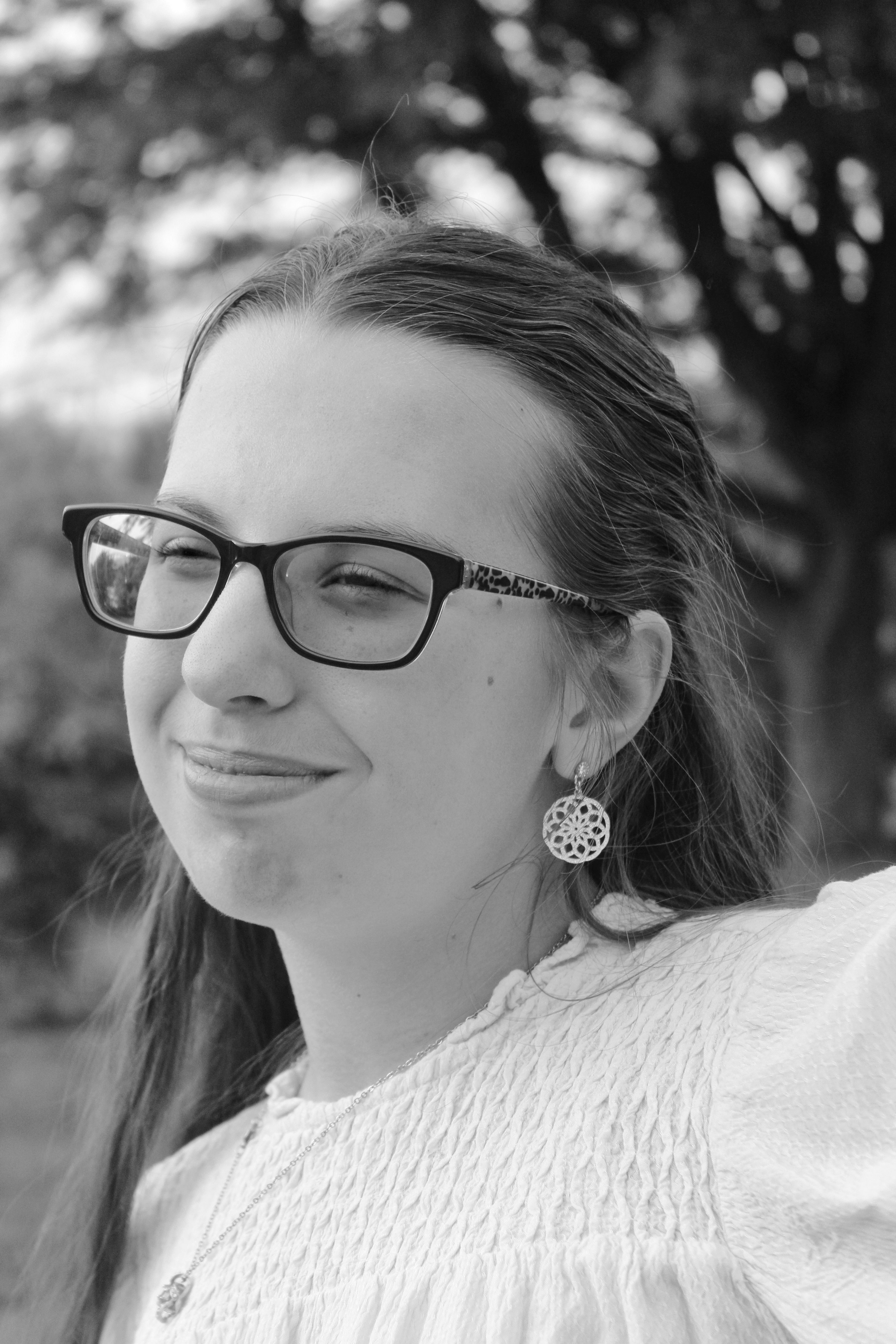 Black and white portrait of a smiling young woman with glasses in an outdoor setting.