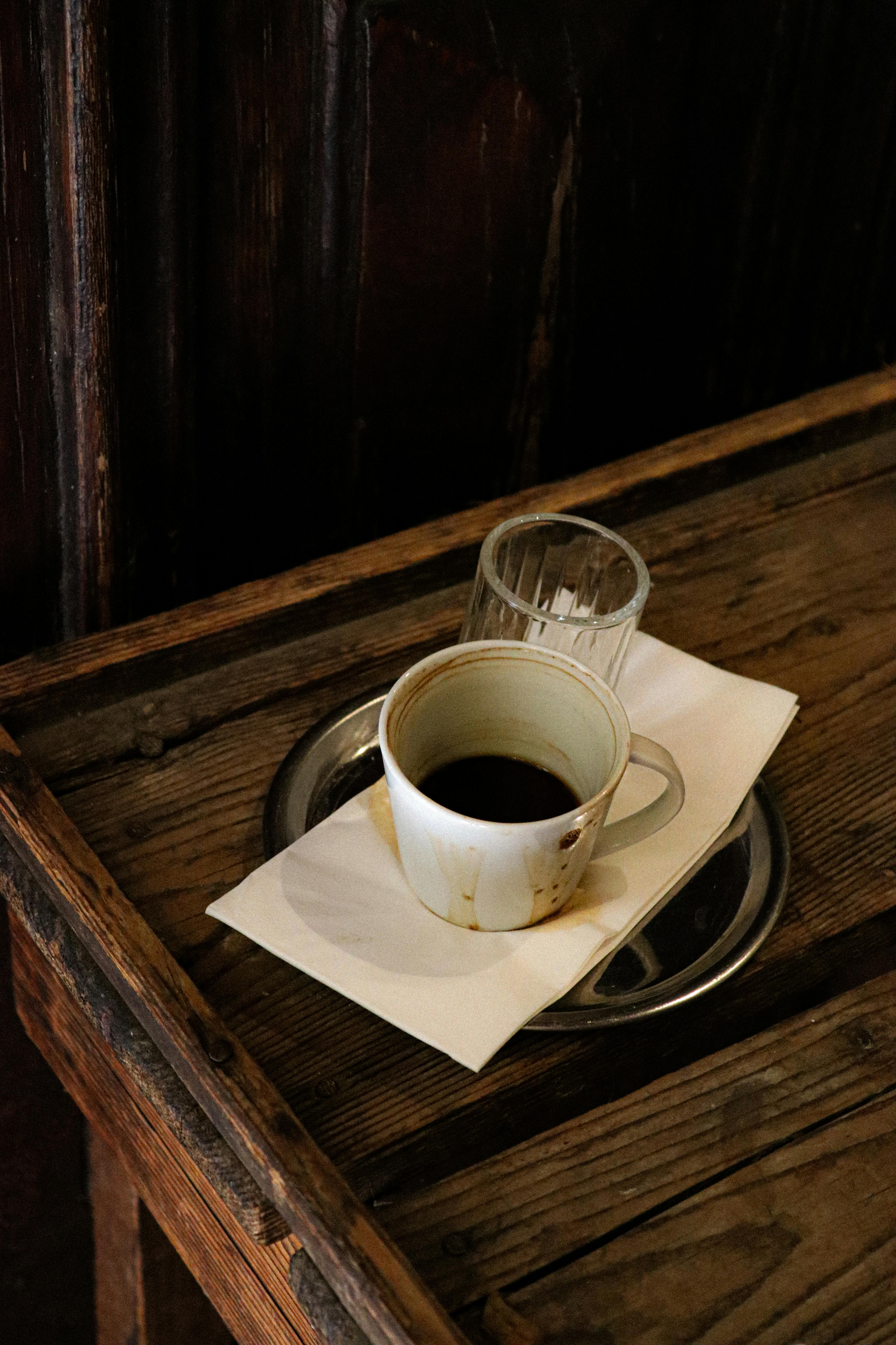 A rustic coffee cup on a wooden table with dim lighting, capturing a warm cafe ambiance.