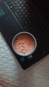 A warm beverage in a mug rests on a black laptop, creating a comfortable and relaxed workspace ambiance.