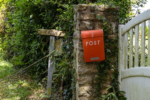 Charming red post box on an ivy-covered stone wall in Brittany, France, near a rustic gate and greenery.