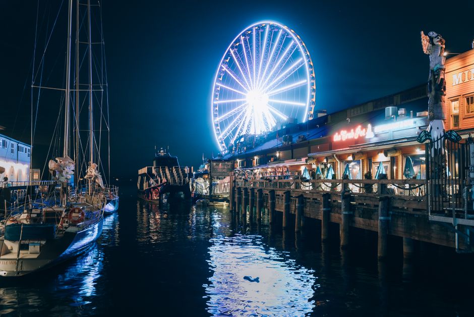 Vibrant night view of Seattle's Great Wheel and waterfront, reflecting city lights.