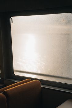 Misty sunlight streaming through a ferry window with reflections on the water, creating a peaceful atmosphere.