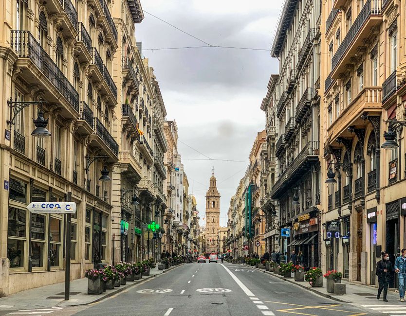 Vista escénica de una calle histórica en Valencia, España, con una prominente torre campanario bajo un cielo nublado.
