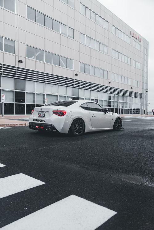 Free White sports car parked outside a modern building on a cloudy day. Stock Photo