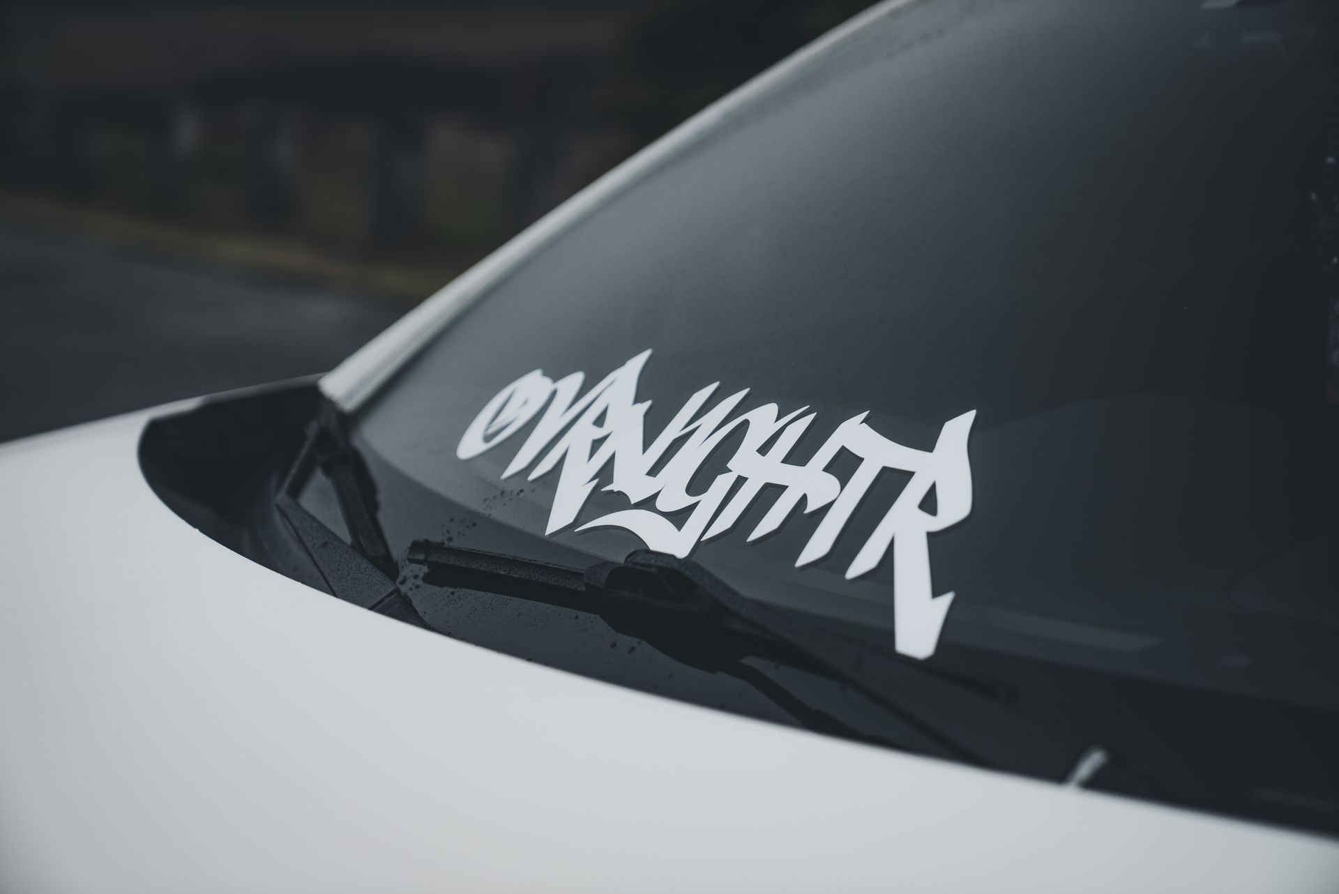Modern angled shot of car windshield featuring bold custom text sticker.