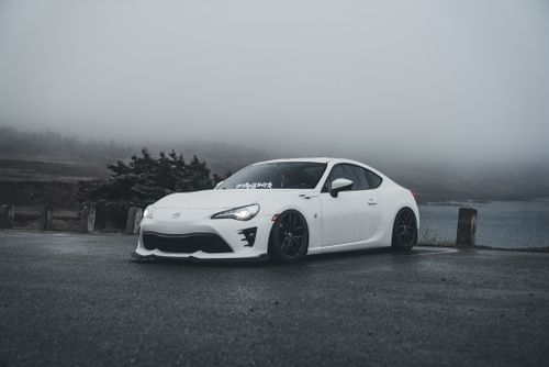 Free White sports car on a foggy day, parked beside a misty lake with mountains in the background. Stock Photo