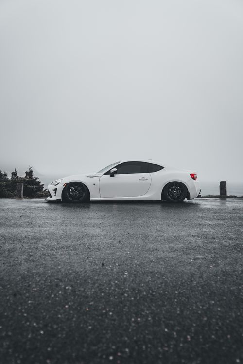Free White sports car parked outdoors on a rainy day, emphasizing sleek design and modern aesthetics. Stock Photo