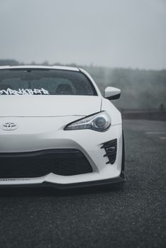 Front view of a sleek white sports car parked outdoors on a cloudy day, highlighting modern design.