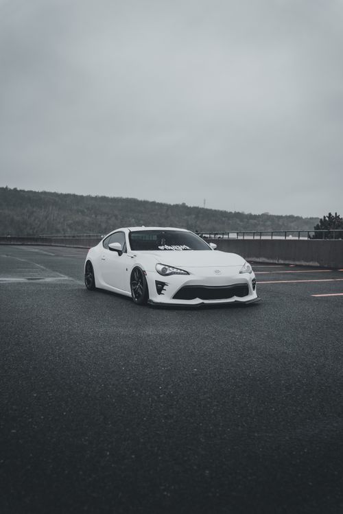 Free White sports car parked on asphalt, captured on a cloudy day. Modern and minimalist setting. Stock Photo