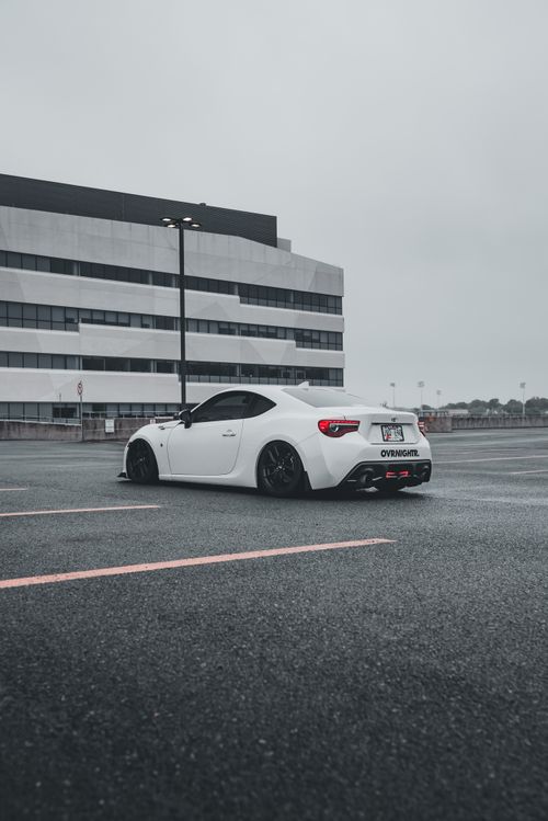 Free A modern white sports car parked in a city lot, showcasing sleek design on a cloudy day. Stock Photo