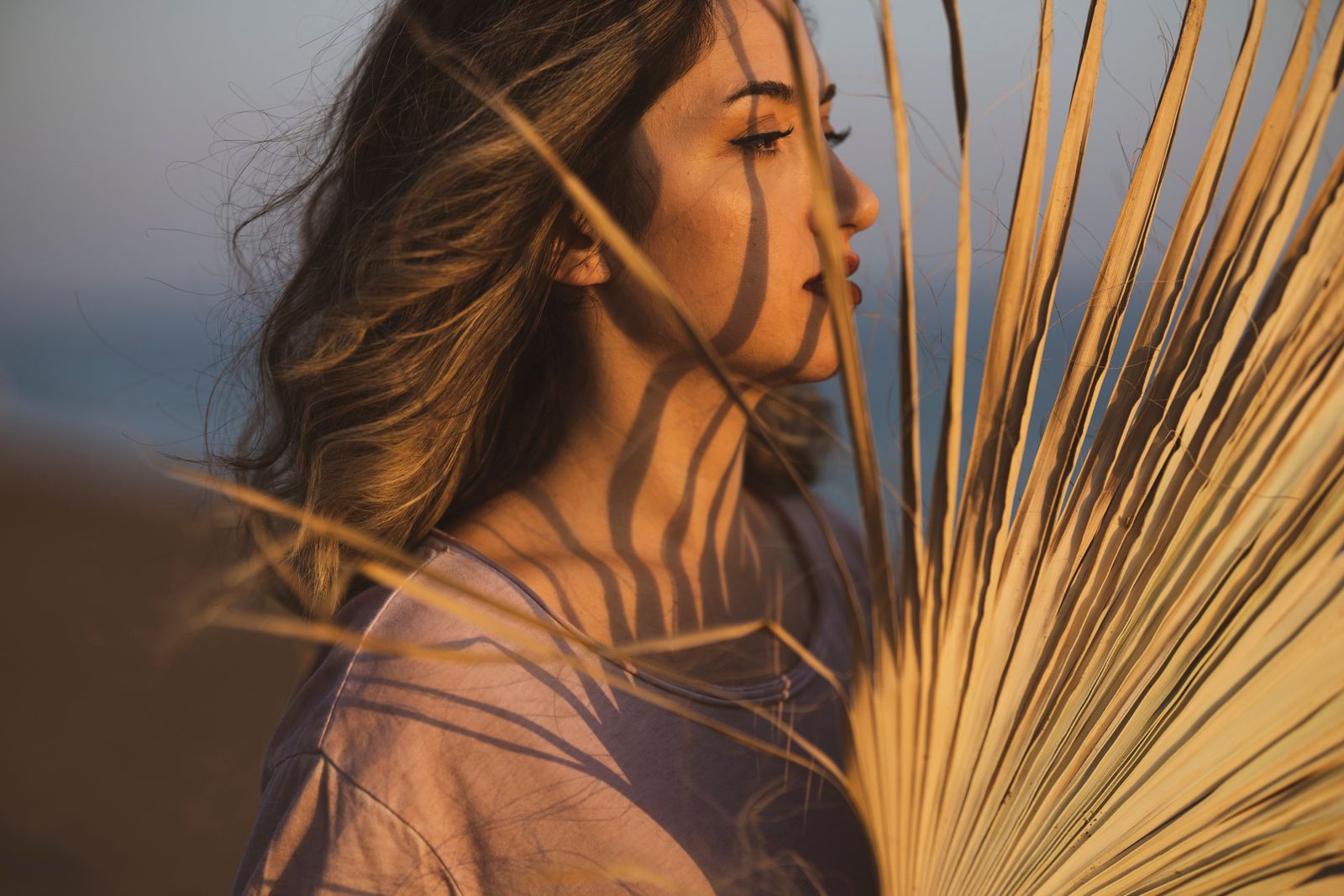 Woman in profile at sunset with palm leaf shadows across her face and neck