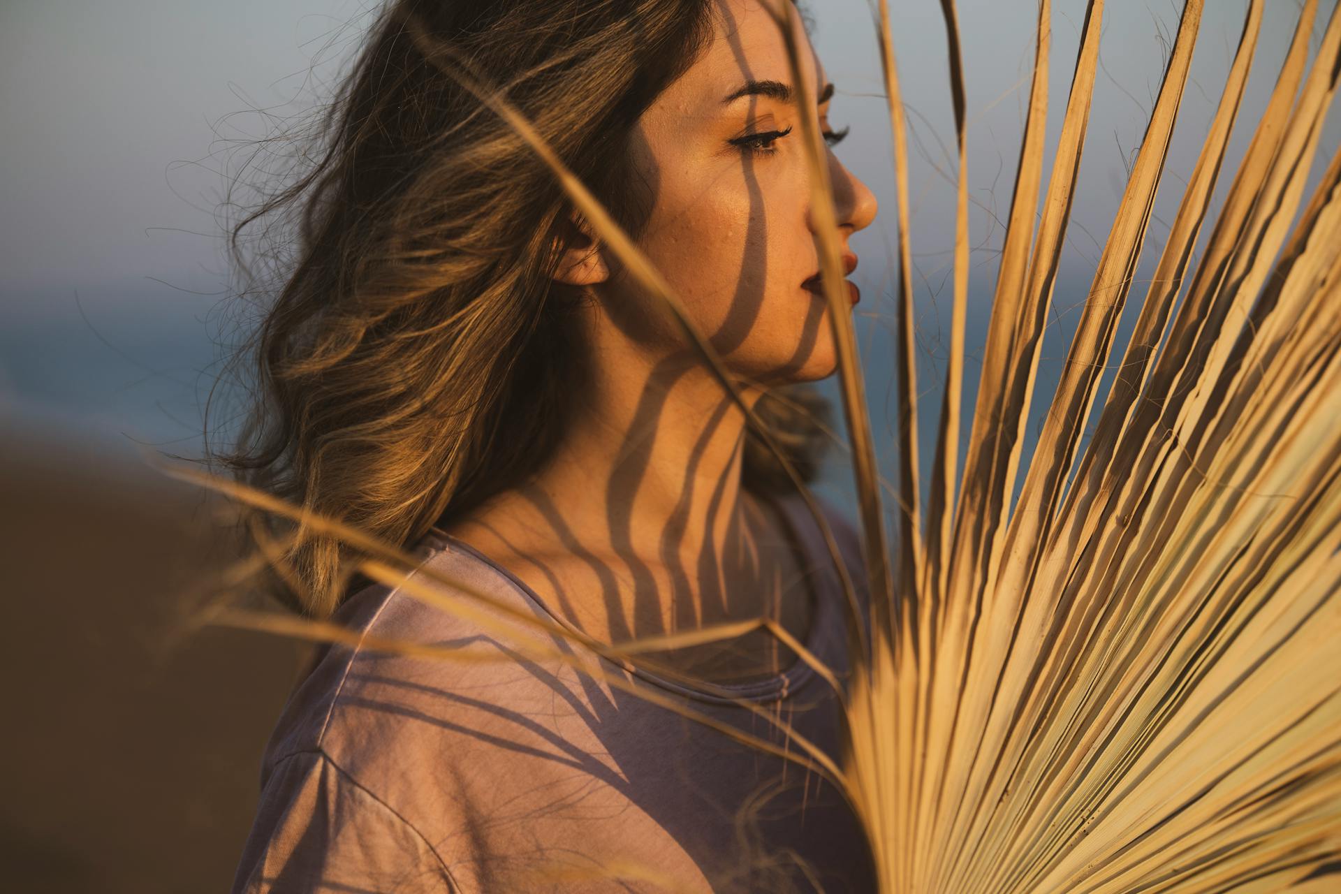 Side profile of a woman with palm leaf shadows on her face at sunset.