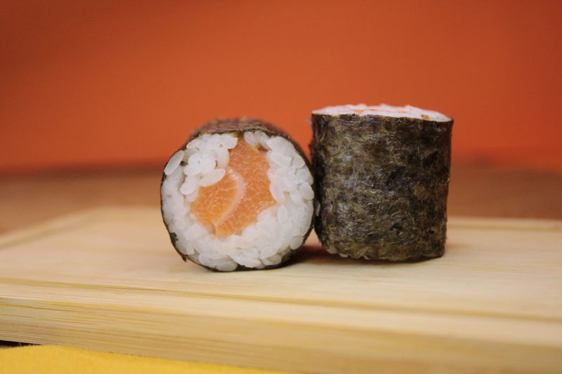 Deux makis au saumon entourés de nori, sur une assiette en bois