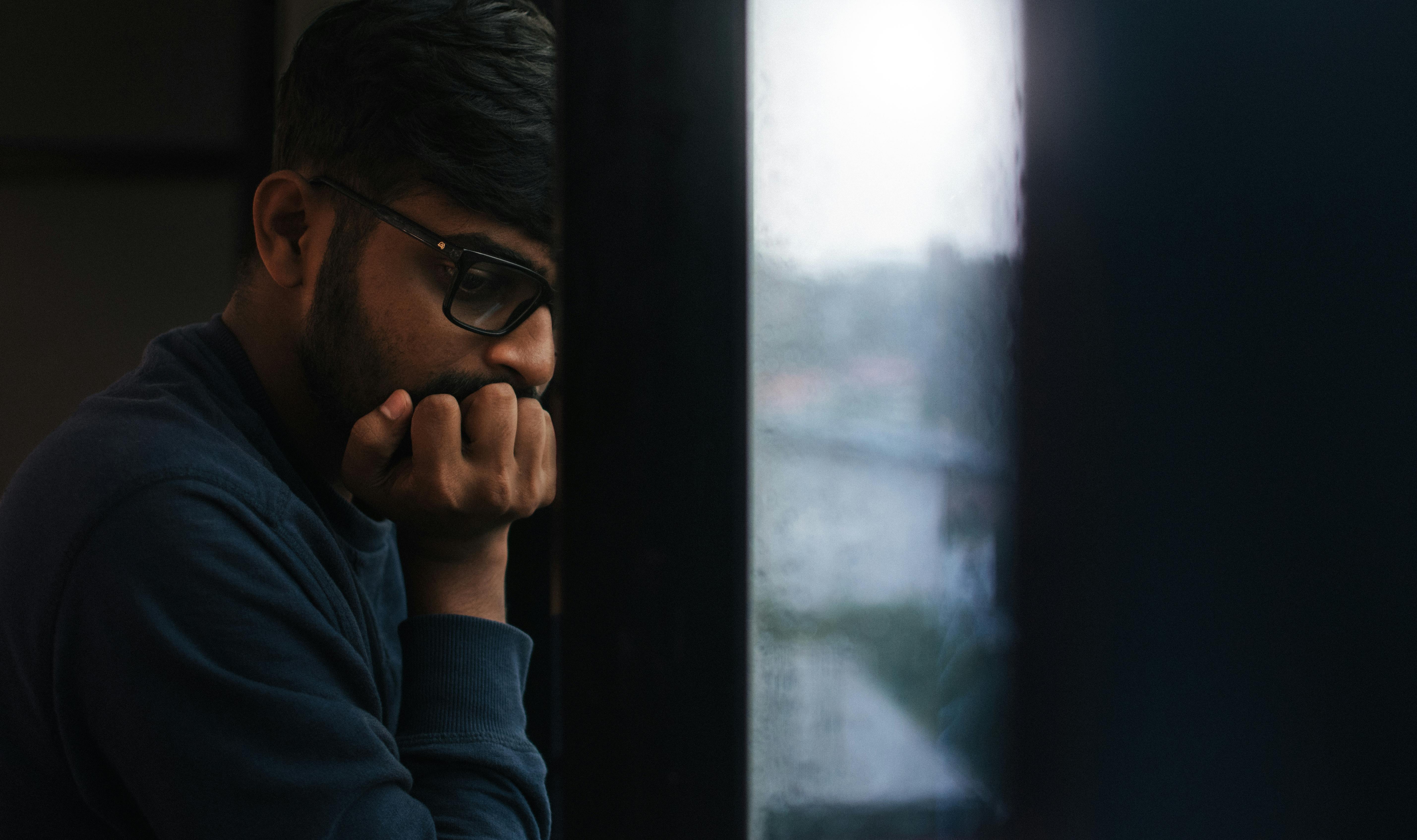 Gratis Hombre contemplativo mirando por una ventana lluviosa, perdido en sus pensamientos. Foto de stock