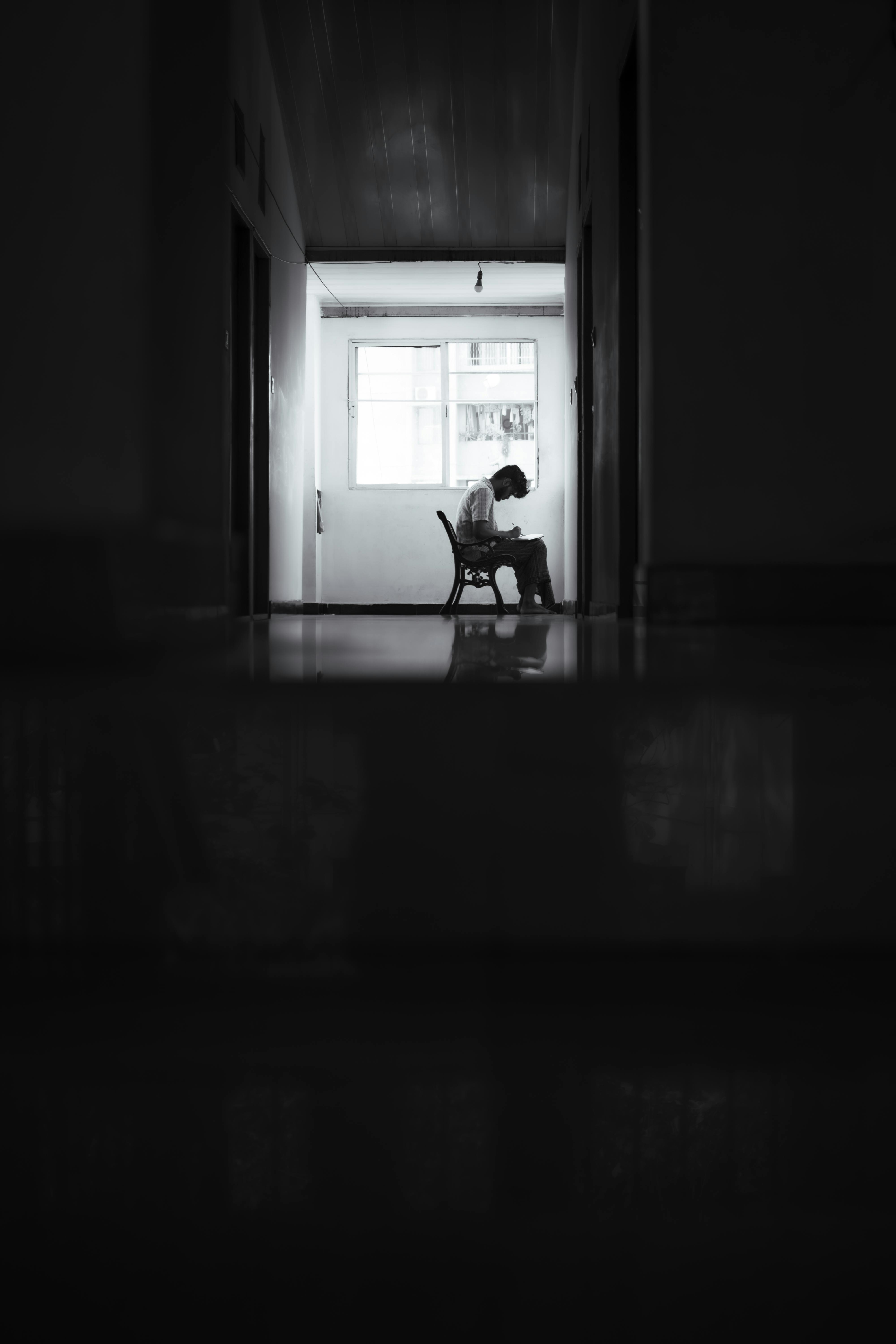 Zadarmo Osamelá postava sedí v tmavej chodbe, osvetlenej prirodzeným svetlom cez okno. Fotka z fotobanky