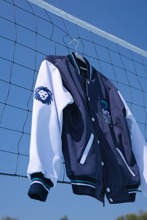 Free A stylish navy blue varsity jacket hangs on a net outside, featuring a lion emblem on the sleeve. Stock Photo