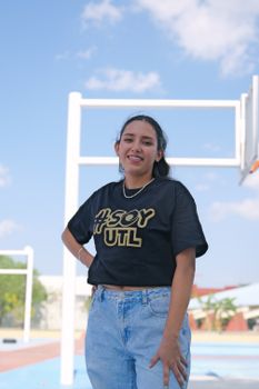 Portrait of a young woman standing outdoors in León, Mexico, with blue sky and basketball hoop in the background.