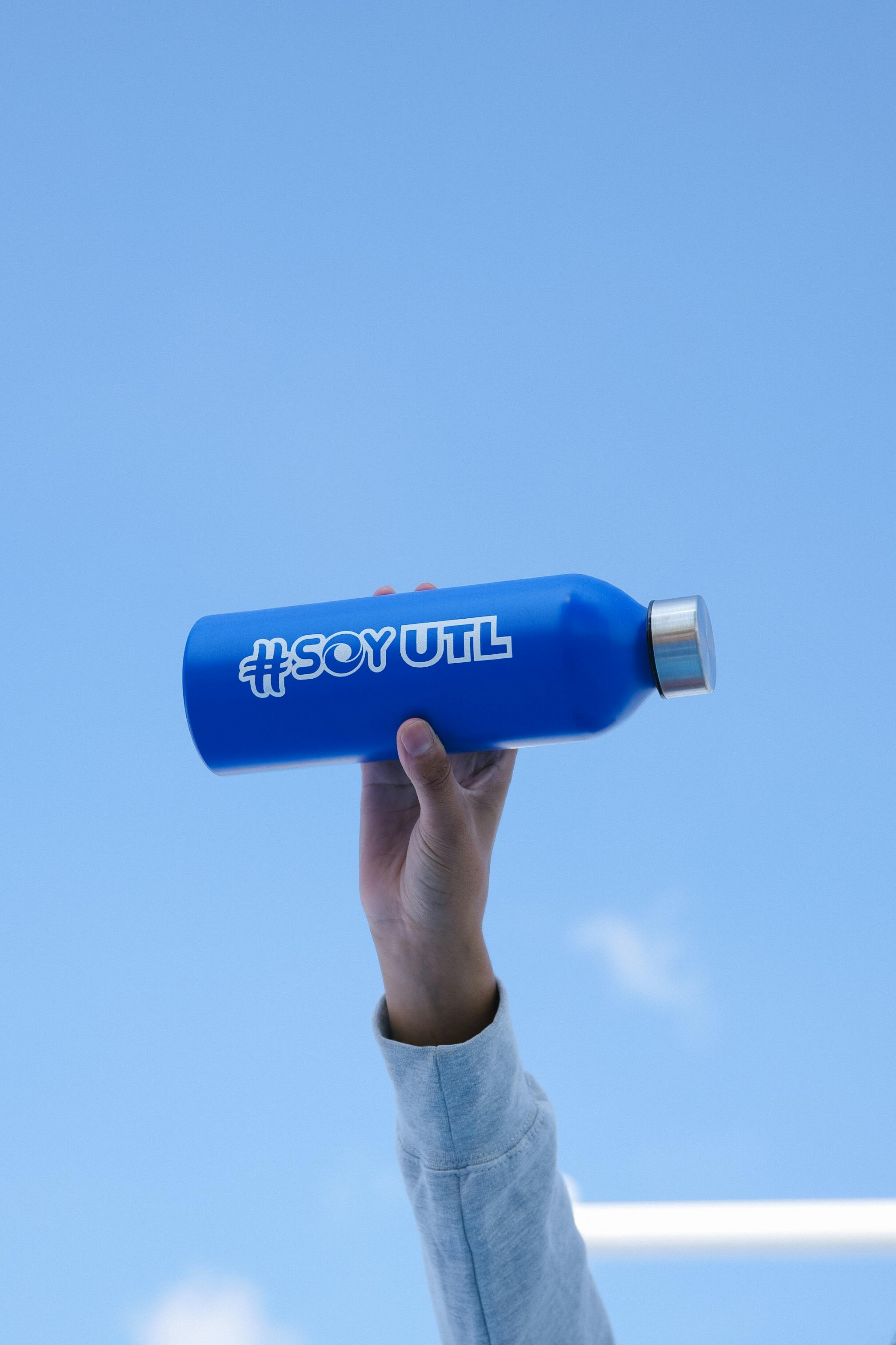 A blue bottle with UTL logo held up against a clear sky, symbolizing freshness.