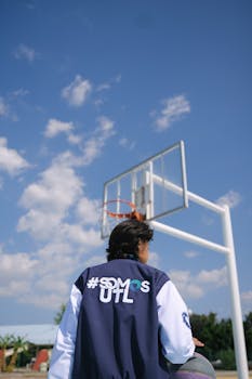 A young man wearing a sports jacket plays basketball outdoors under a clear blue sky.