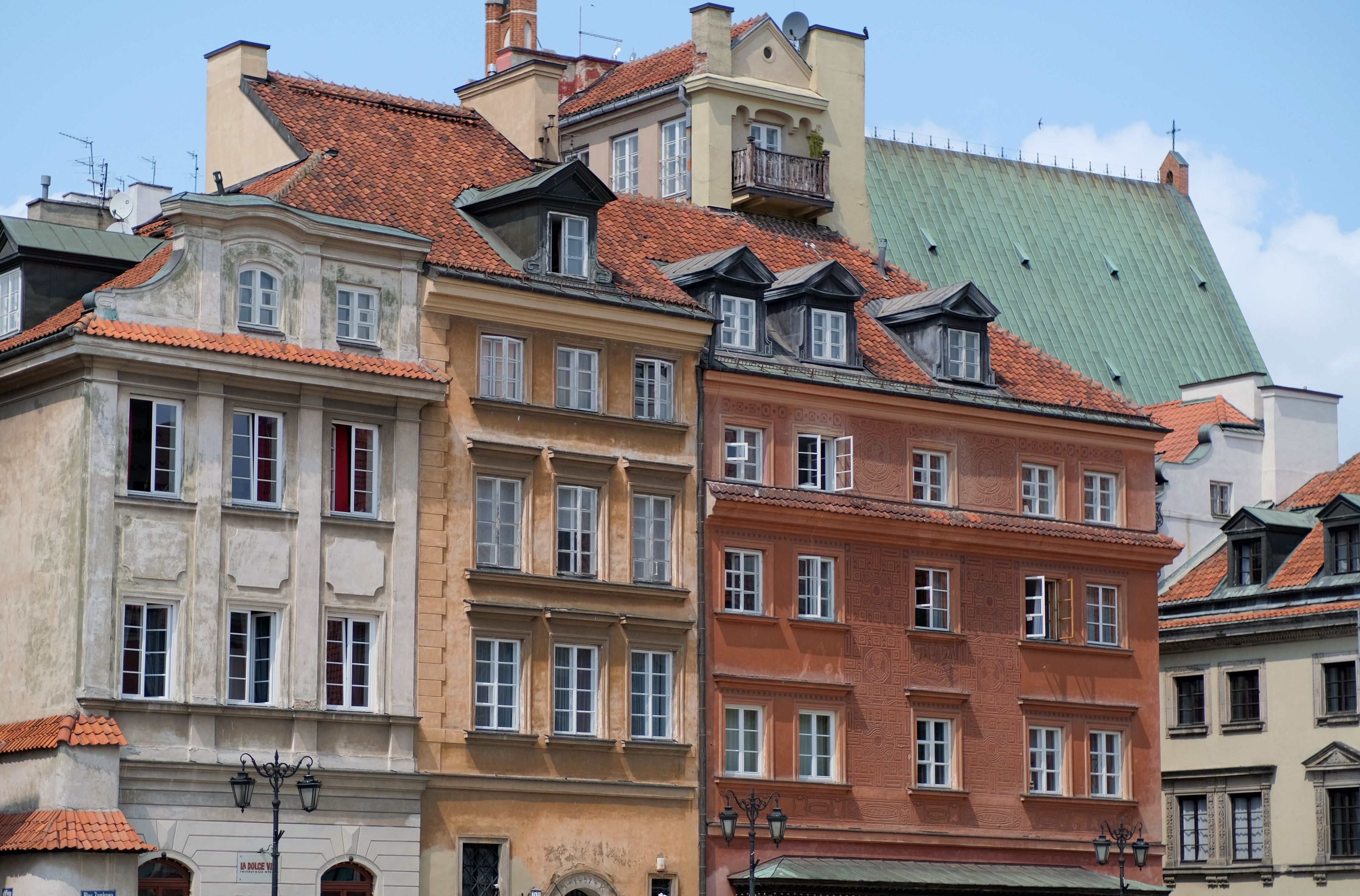 Elegant historical buildings with red-tiled roofs in Warsaw's Old Town on a sunny day.